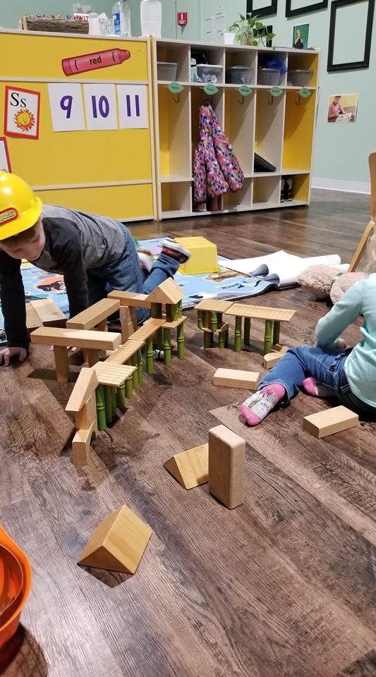Child in yellow hard hat playing with wooden blocks on the floor