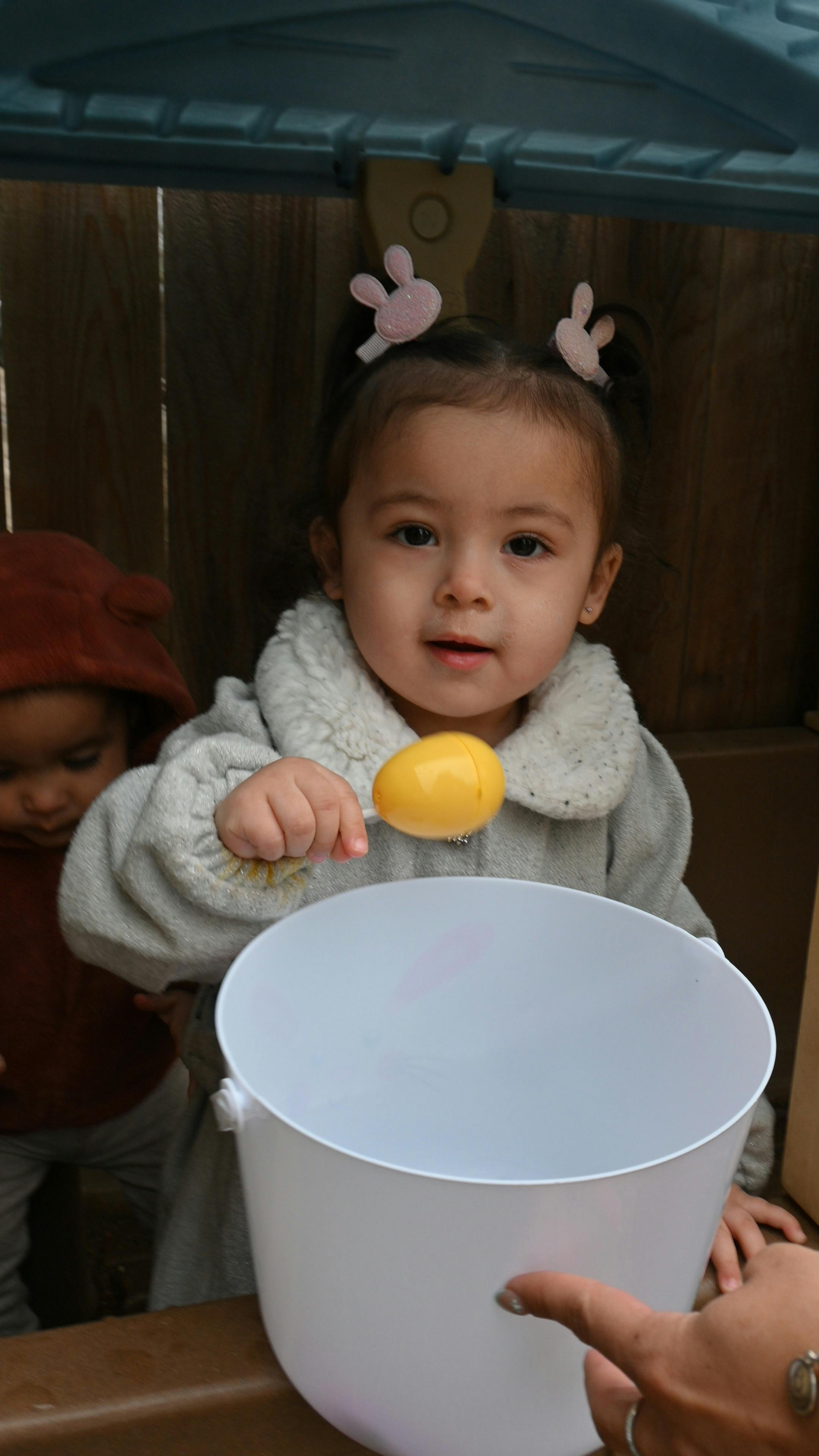 Child holding a yellow plastic egg over a white bucket