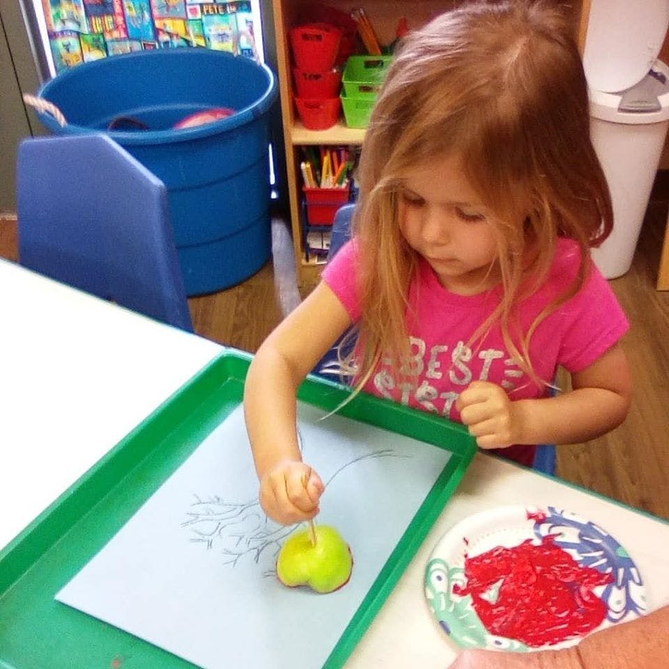 Child using an apple to paint on paper