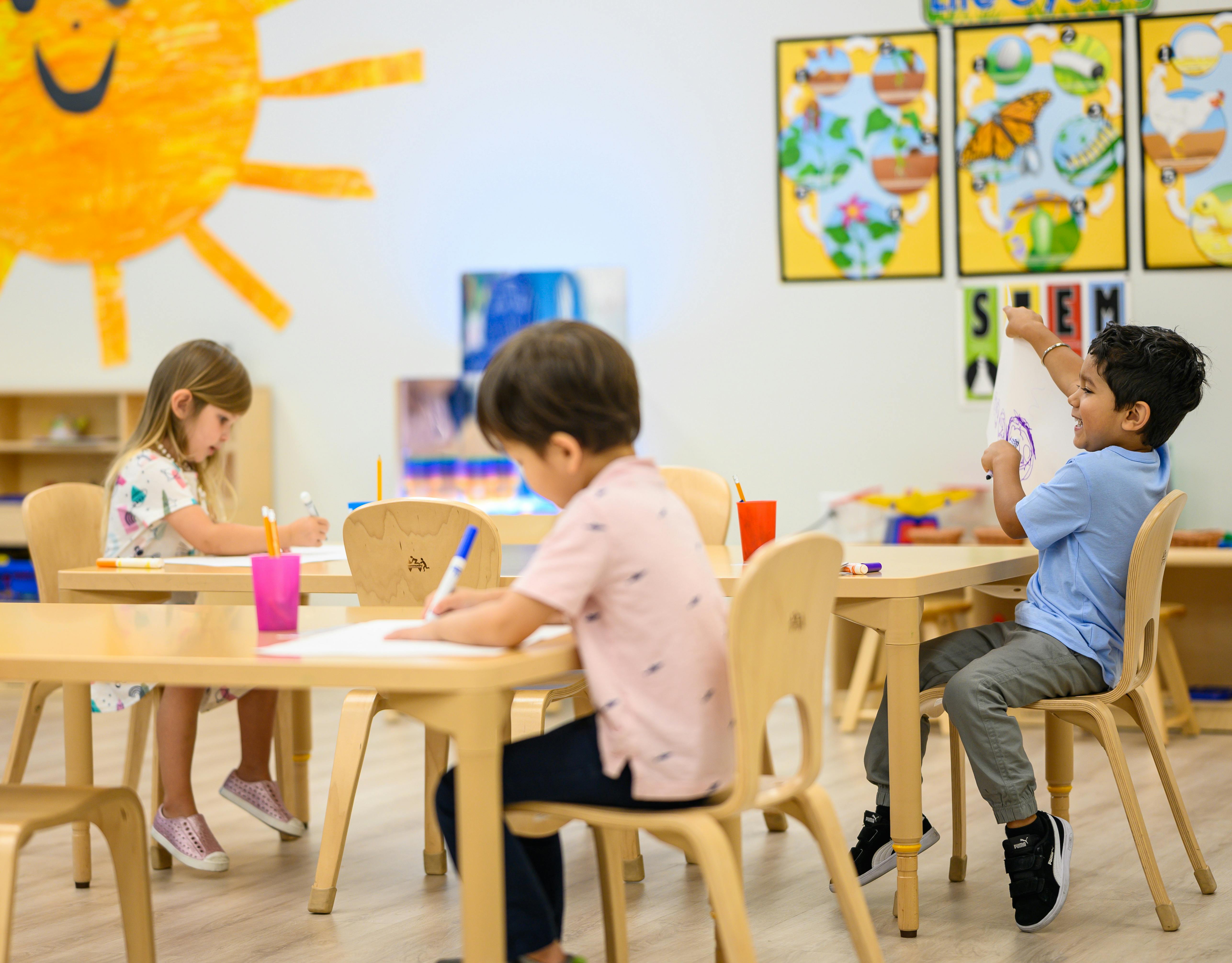 Three children drawing and interacting in a classroom