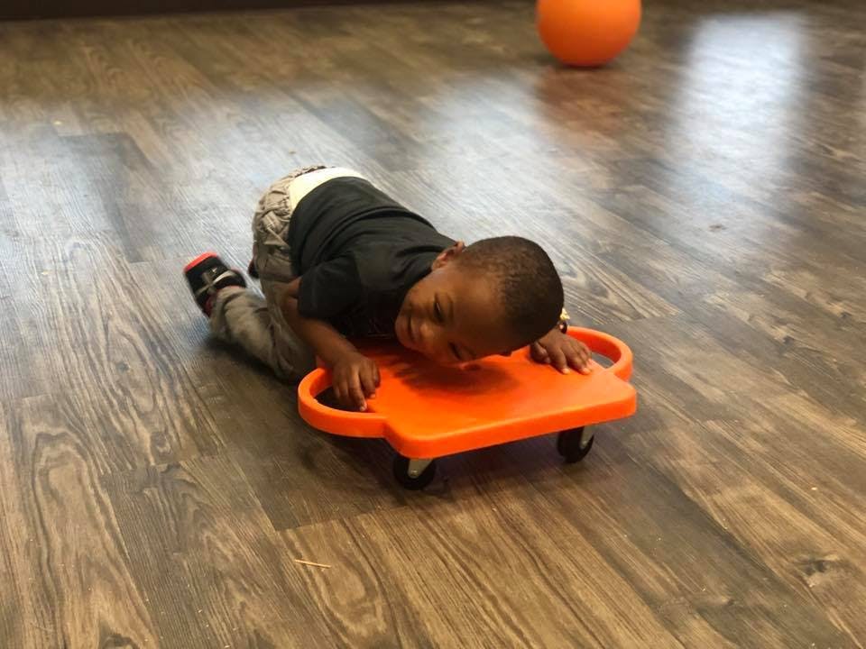 Child on an orange scooter board on a wooden floor
