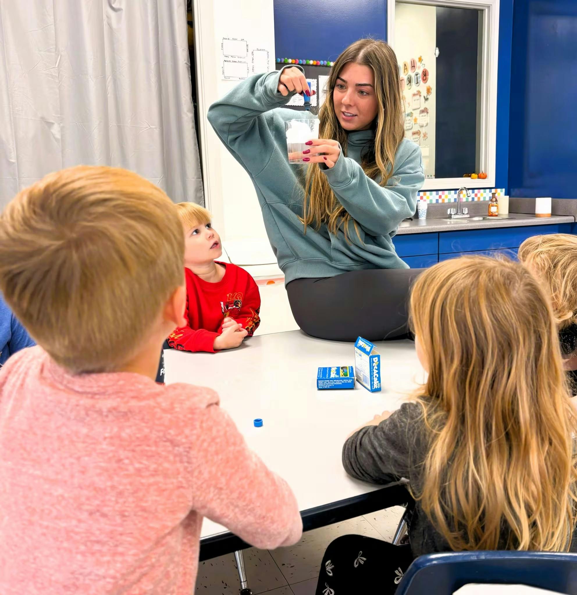 Teacher demonstrating an experiment with liquid and a cup for children in a classroom