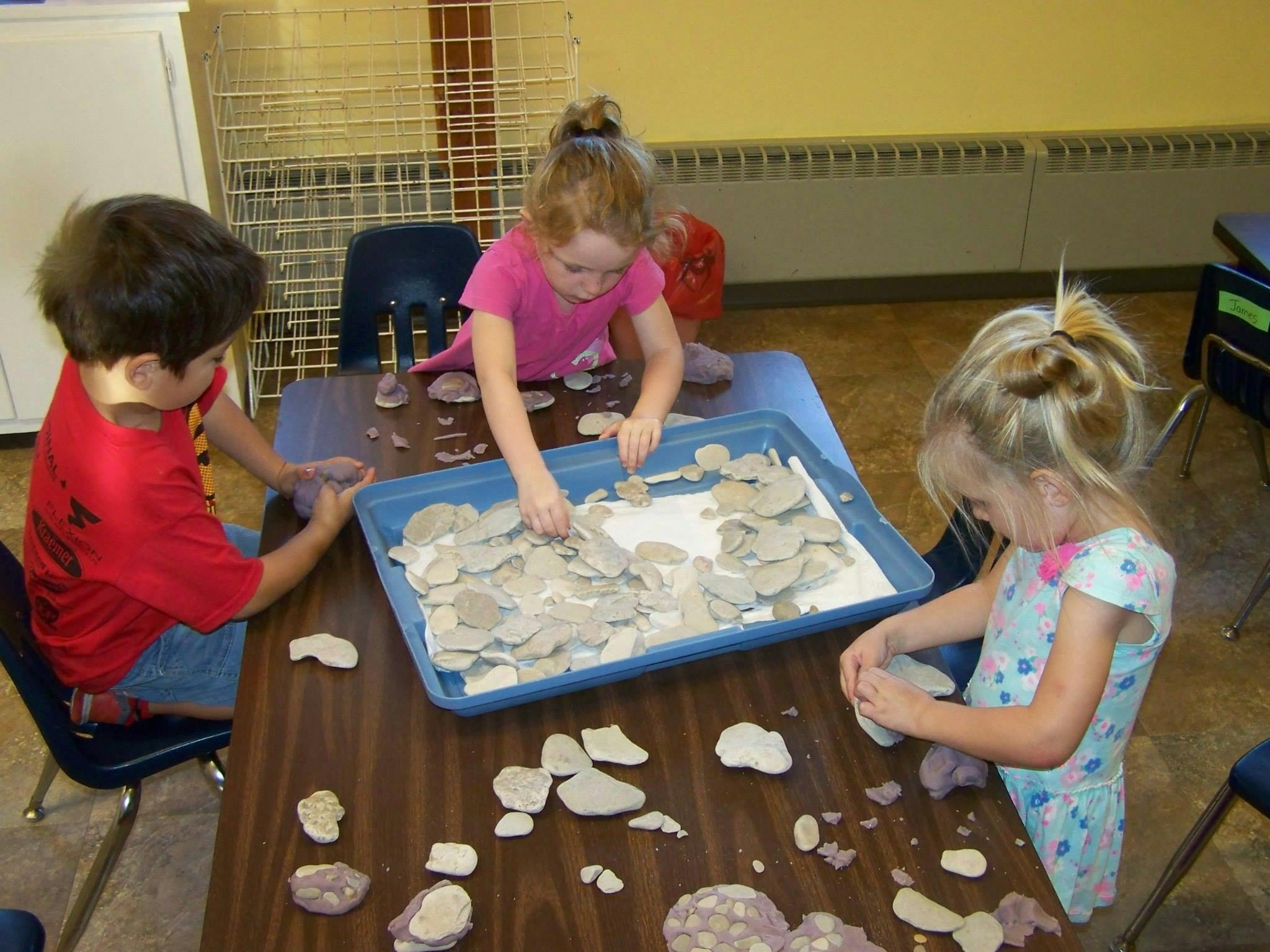 Three children playing with small rocks on a table