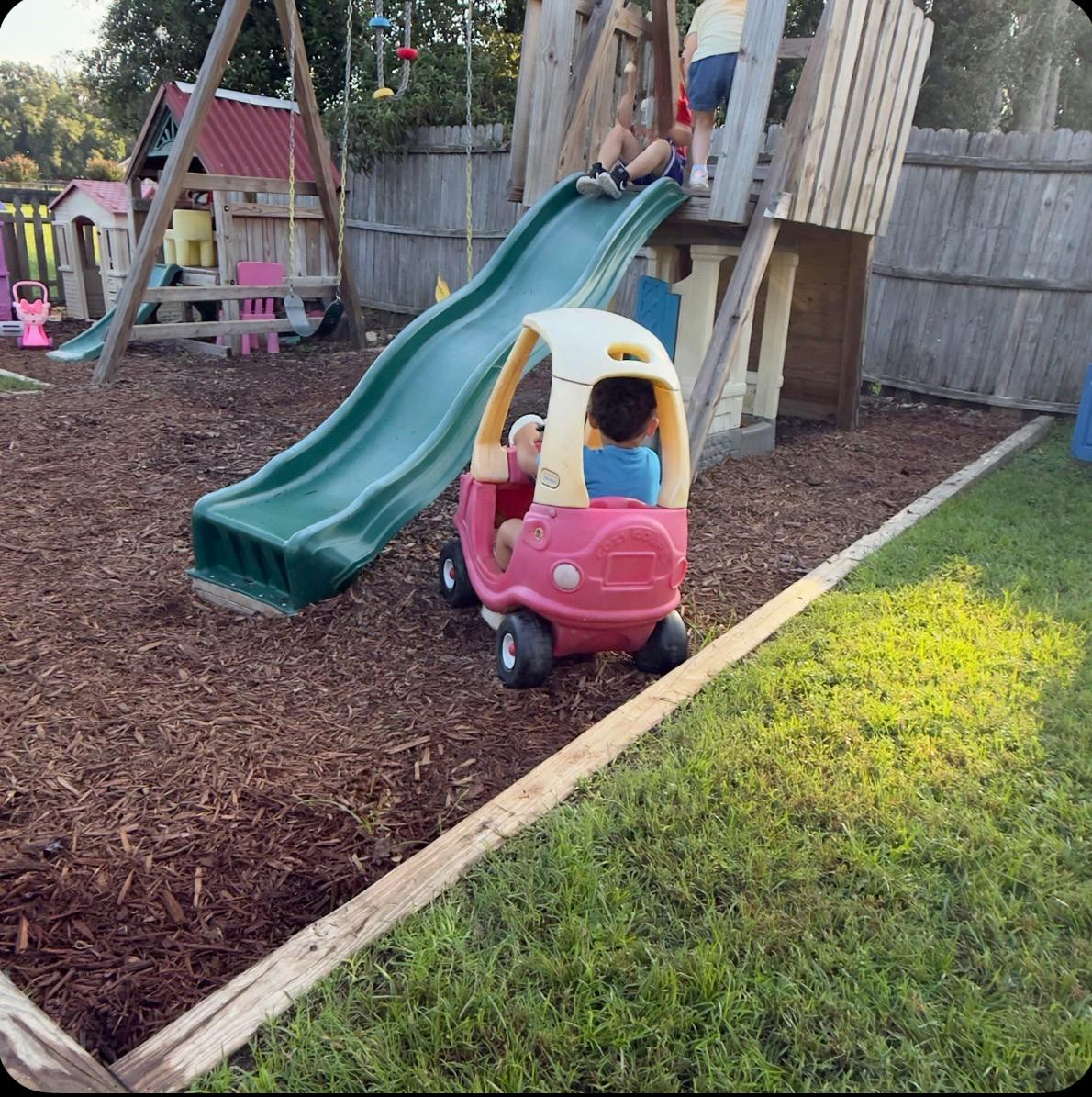 Children playing on a backyard playground with a slide and toy car