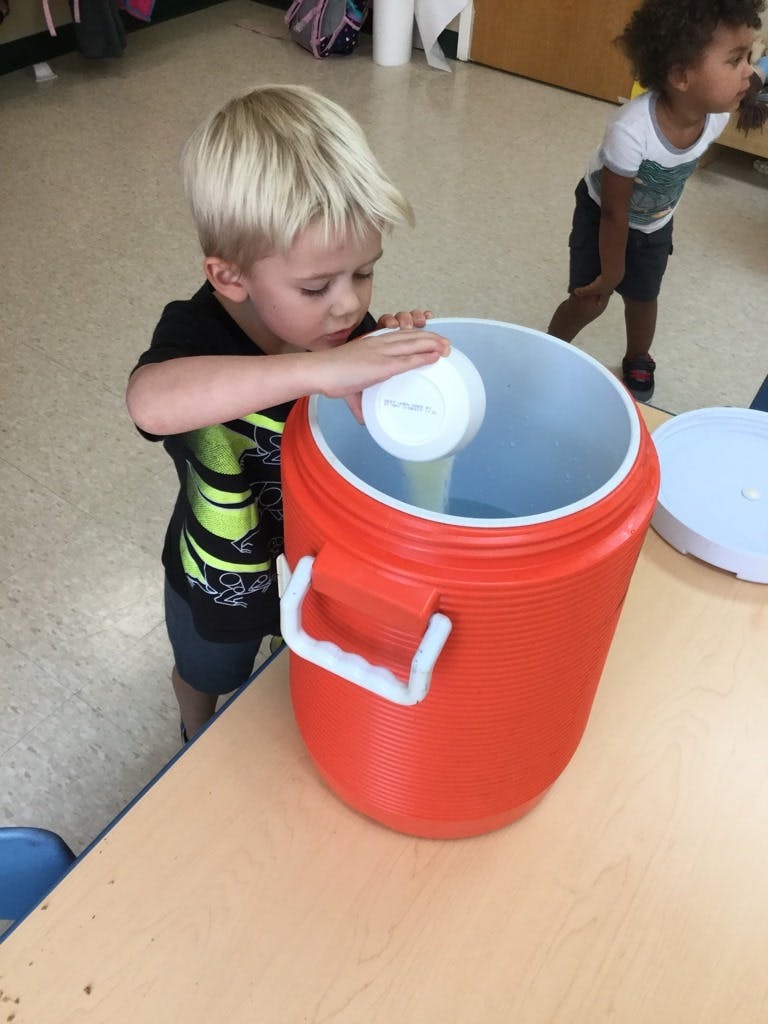 Child putting a white cup into a large red cooler
