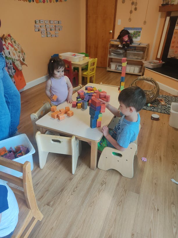 Two children playing with colorful wooden building blocks at a table