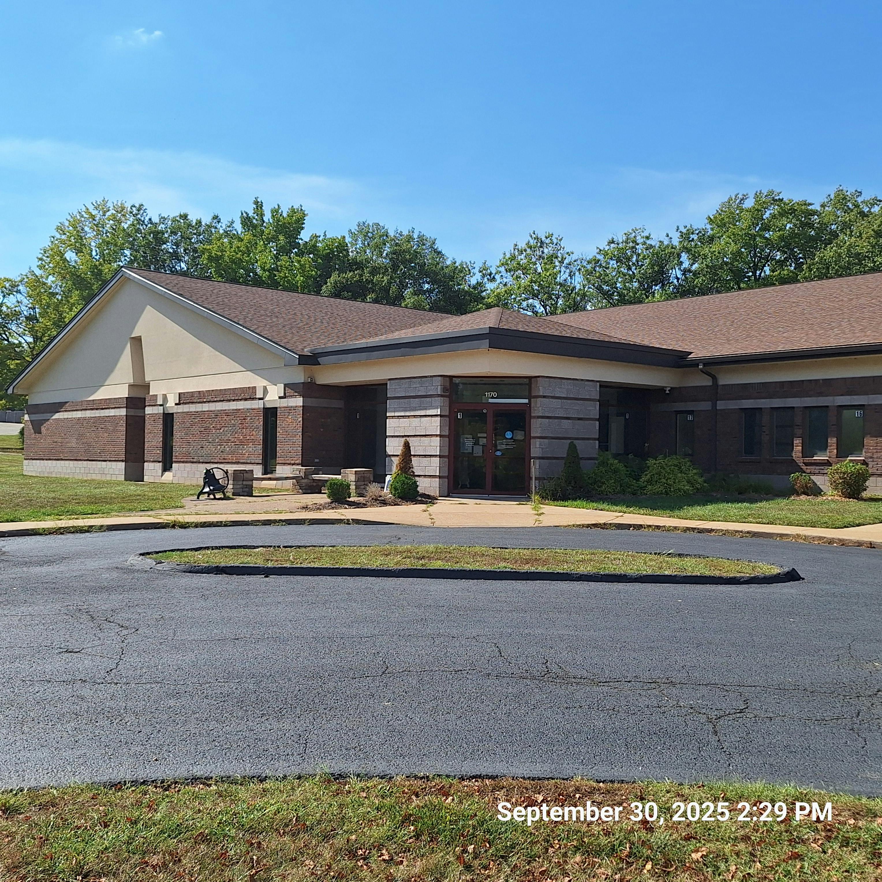 Building with brick and siding exterior, asphalt driveway in foreground