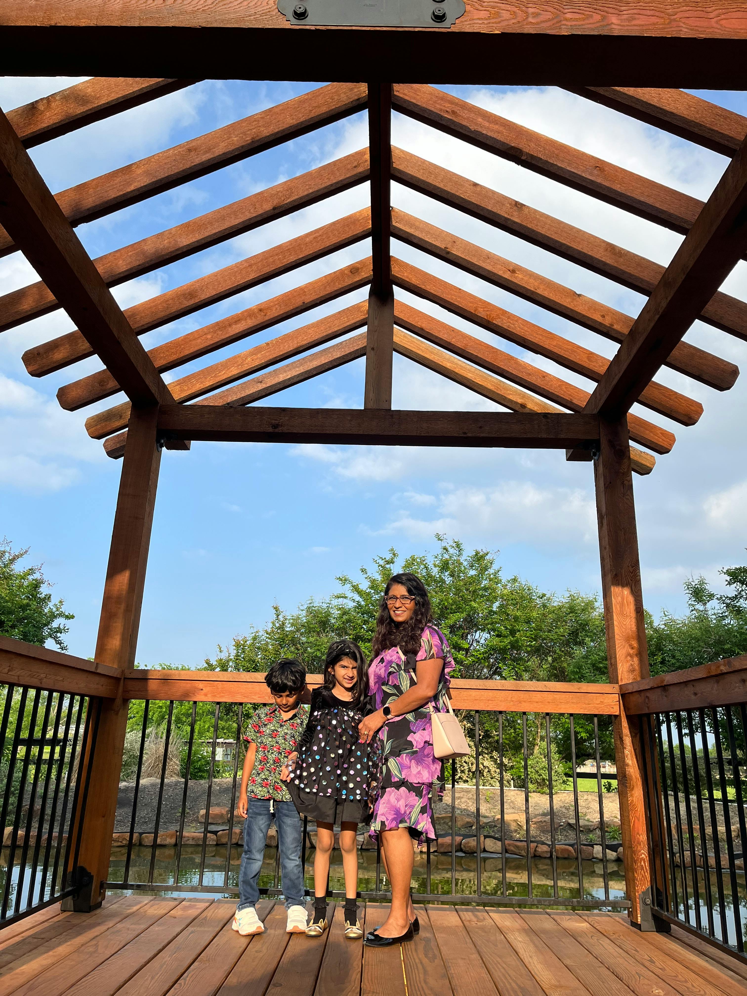 Person and two children standing under a wooden pergola