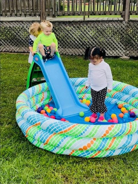 Three children playing with a slide and ball pit outdoors