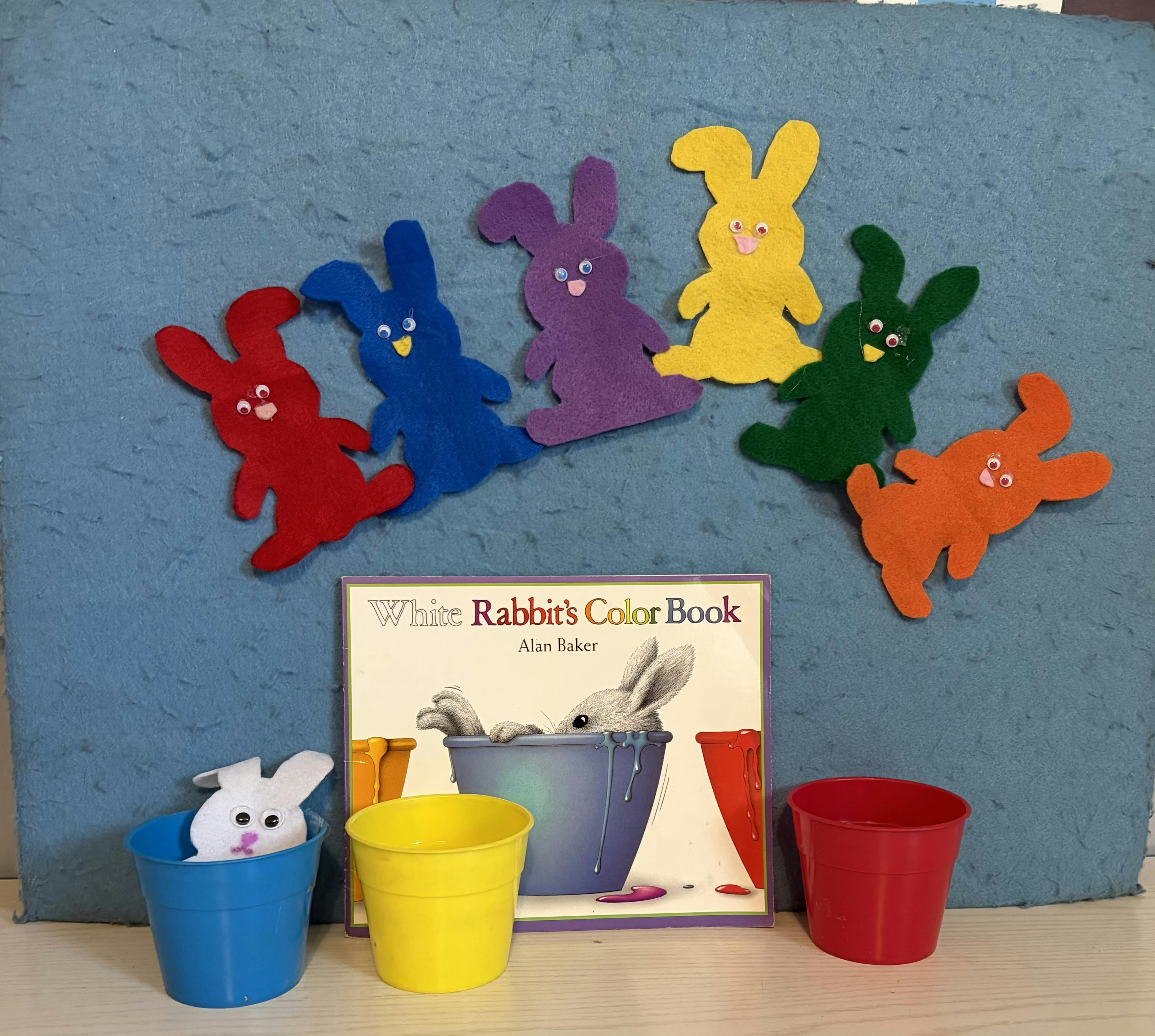 Colorful felt rabbits on a blue board, a book, and colorful plastic cups