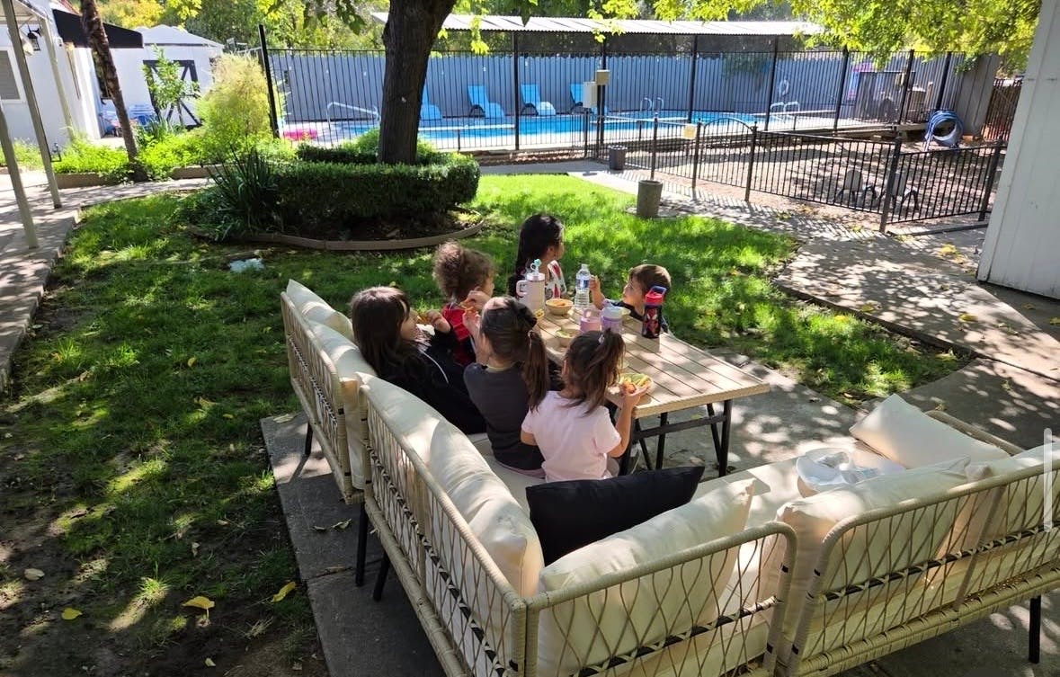 Group of children eating at an outdoor patio table near a swimming pool