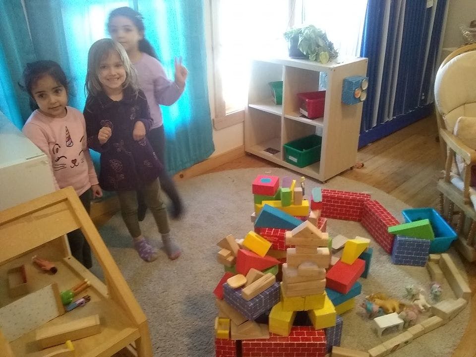 Three children standing near a pile of colorful building blocks