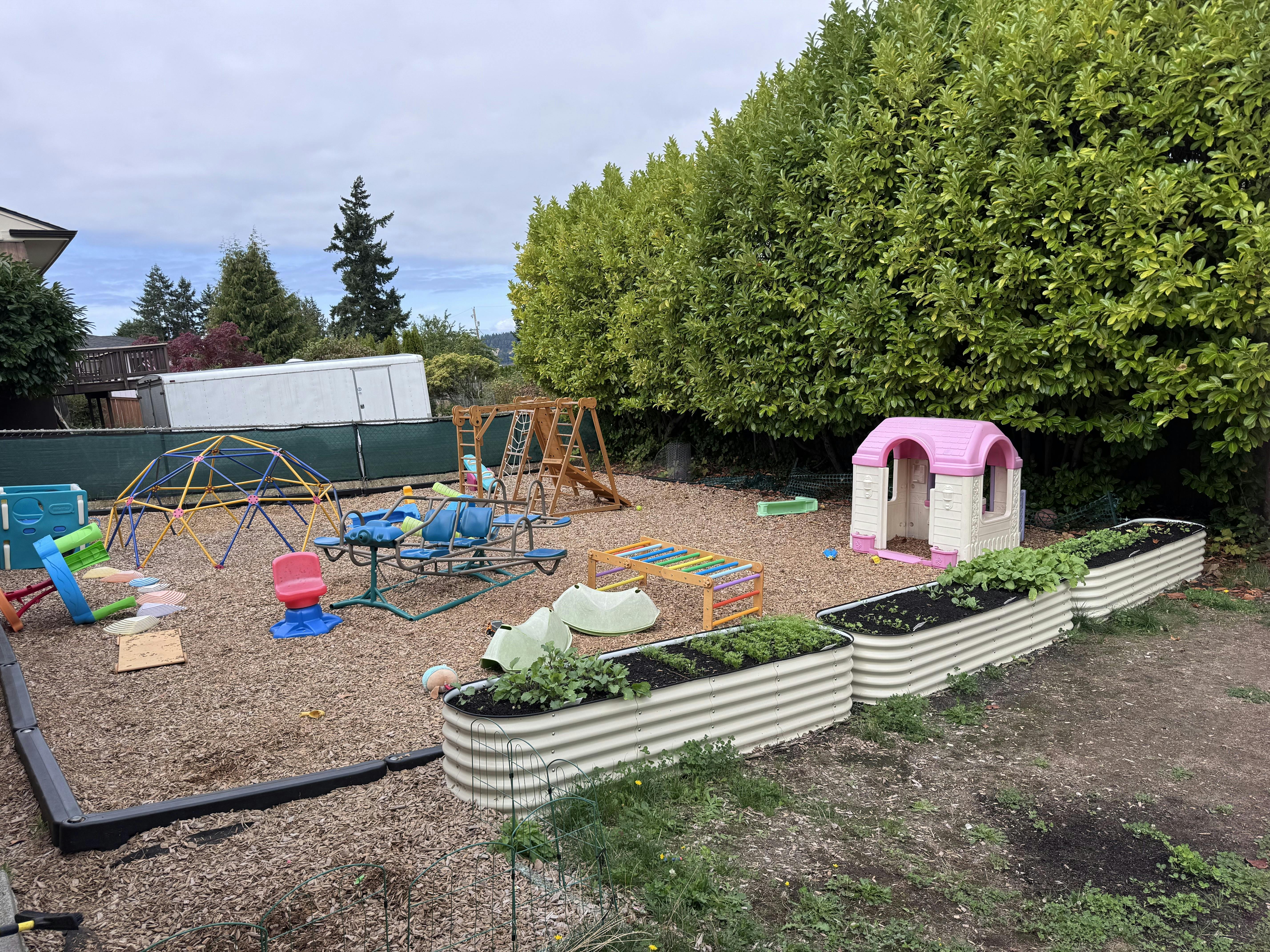 Outdoor playground with various play equipment and raised garden beds
