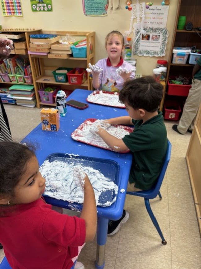 Three children playing with white foam in a classroom