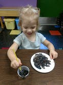 Child playing with black beans and a small cup