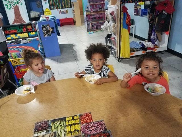 Three children sitting at a table with bowls and spoons