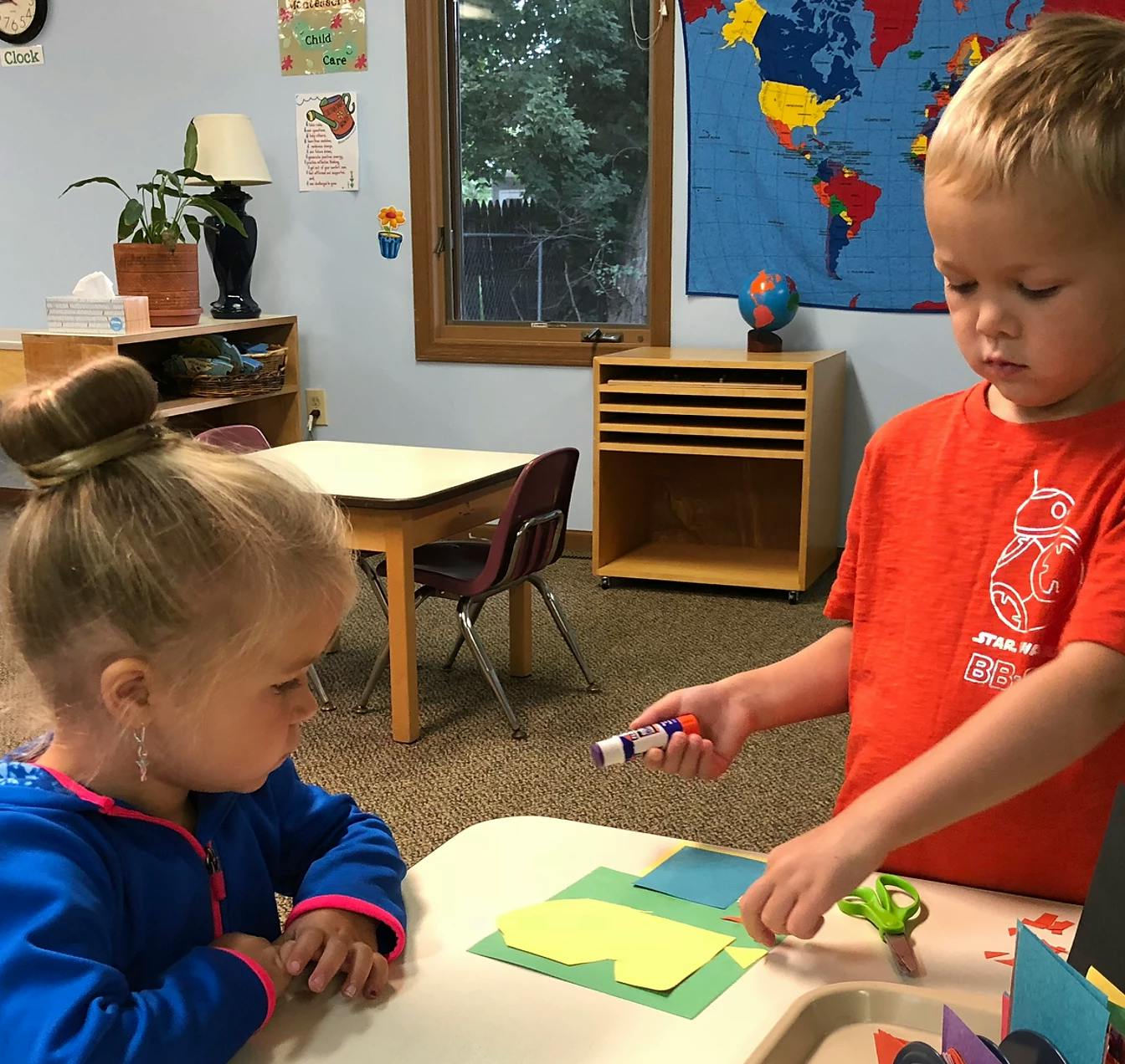 Two children doing crafts at a table in a classroom
