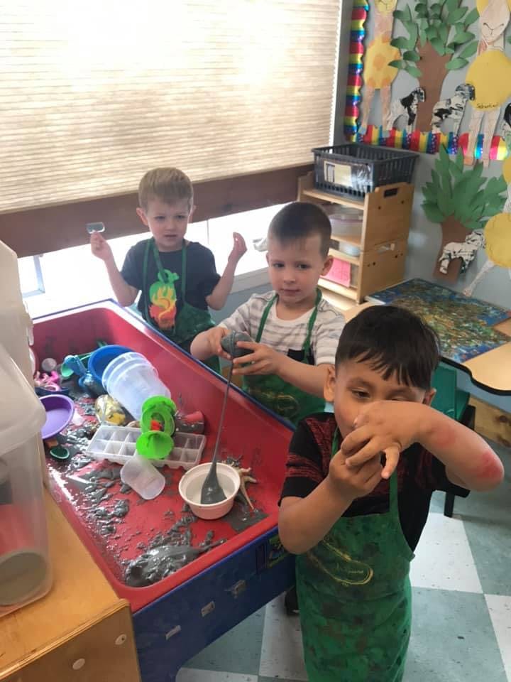 Three children playing at a sensory table in a classroom