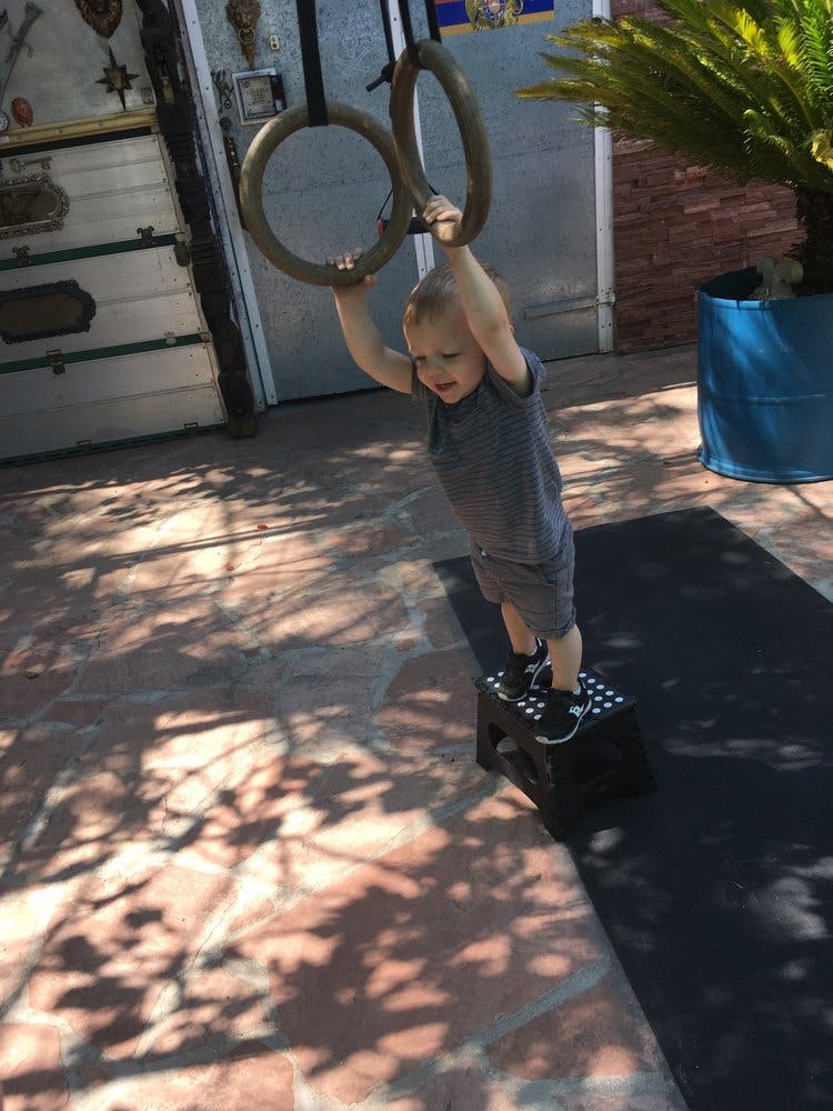Child standing on a stool and holding onto gymnastic rings