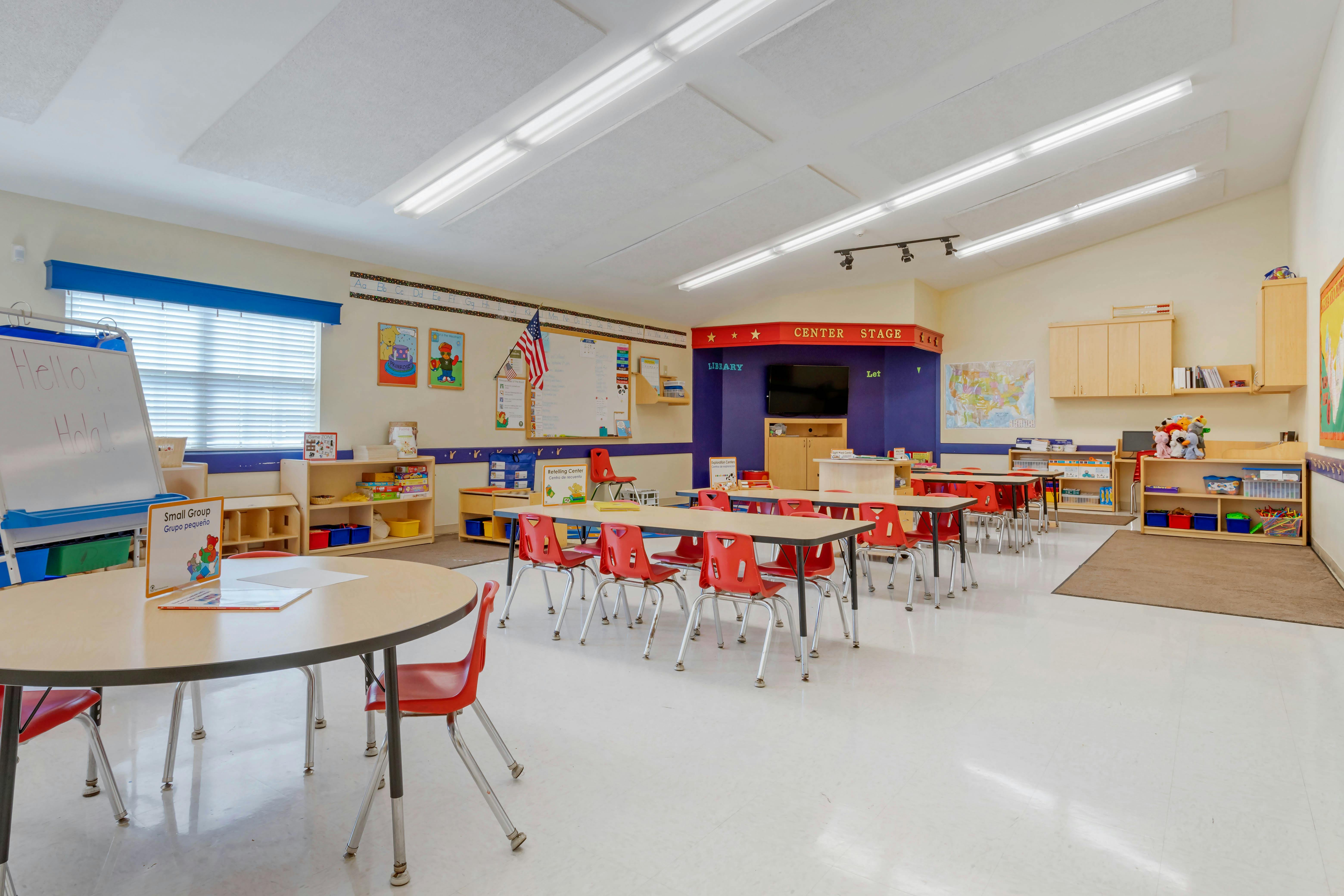 Classroom with small tables and red chairs, whiteboard, and colorful learning aids