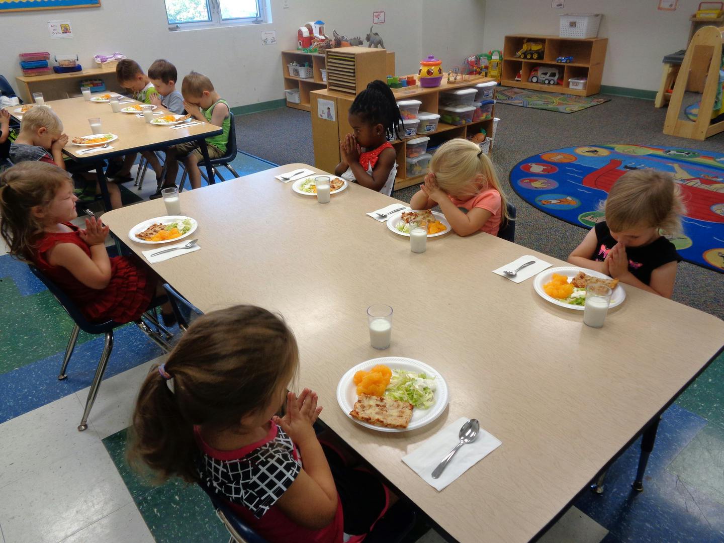 Children sitting at tables with plates of food in a classroom