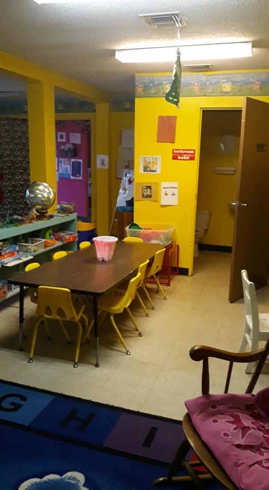 Classroom with a long table and yellow chairs, blue rug, and yellow walls