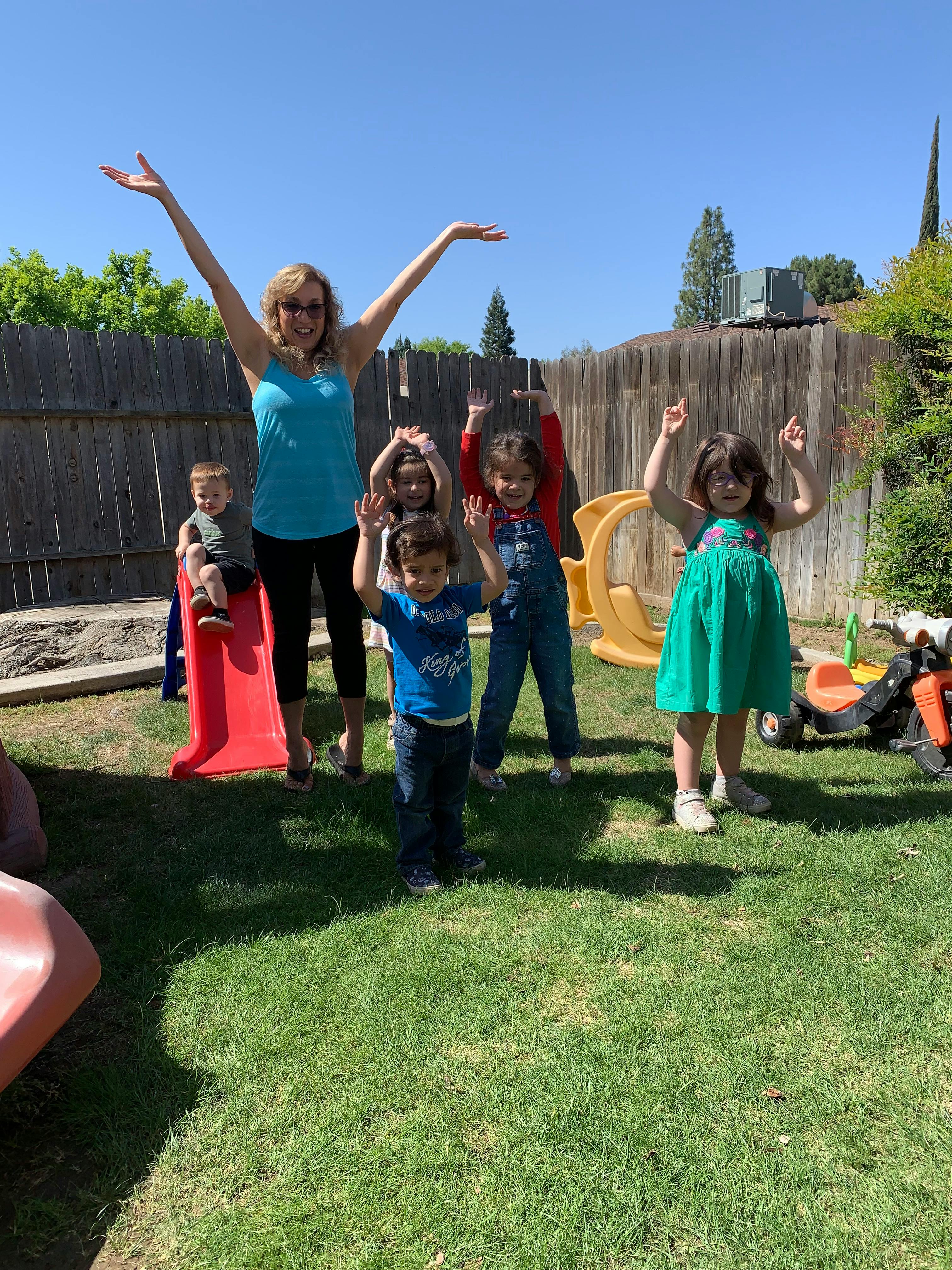 Adult and multiple children posing with arms raised in a grassy yard