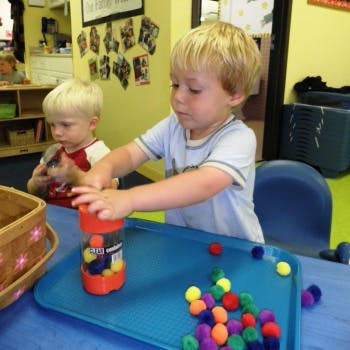 Child playing with colorful pom-poms and a container