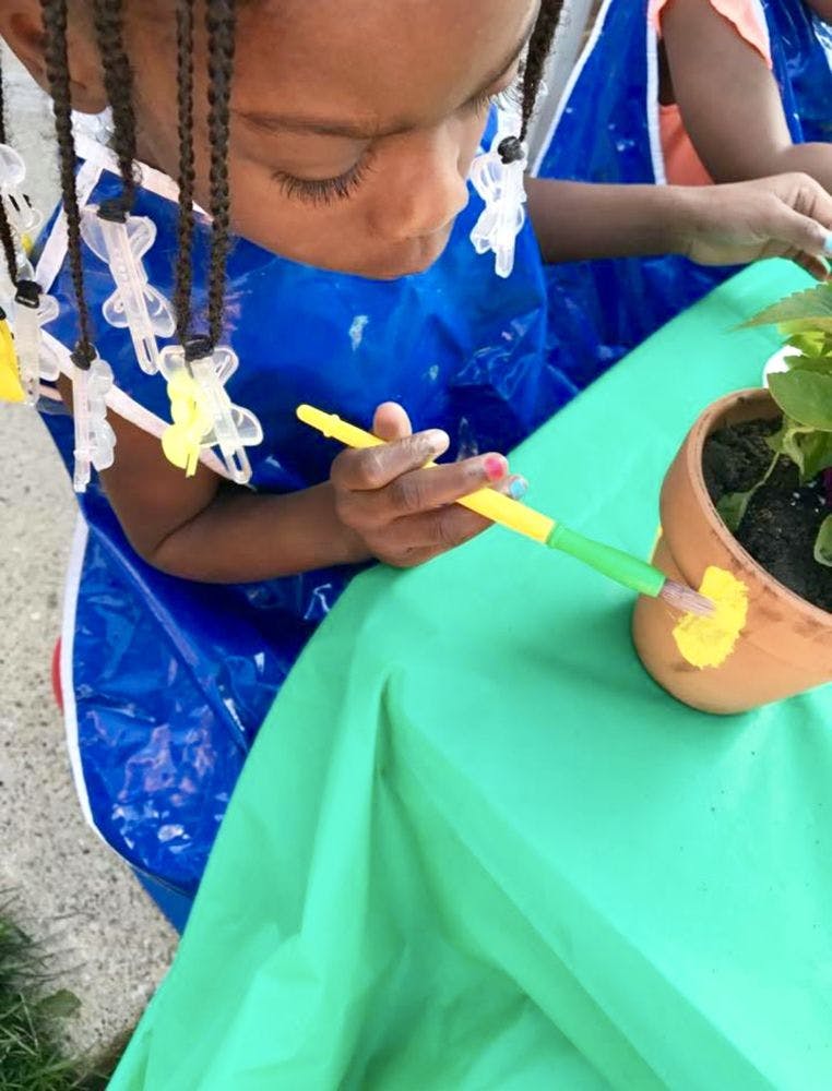 Child painting a terracotta pot with yellow paint