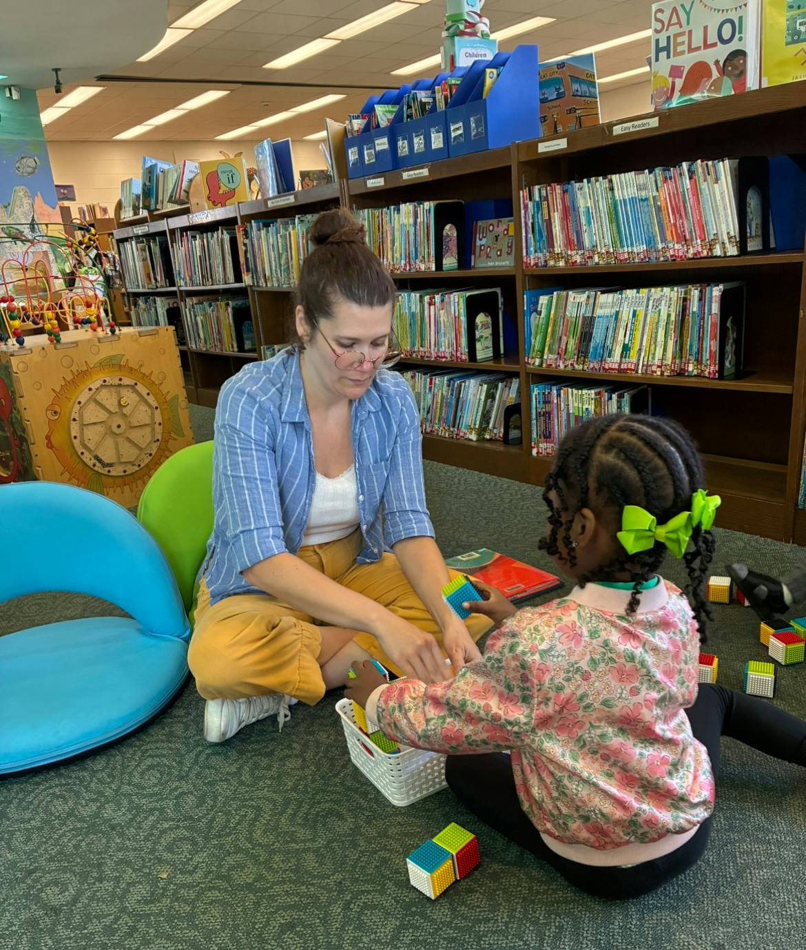 Person and child playing with blocks on the floor in a library