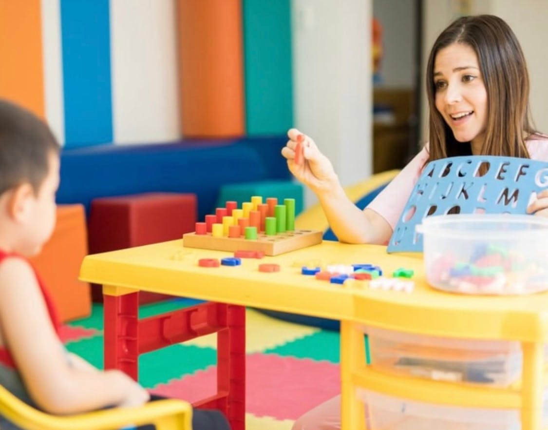Person and child playing with blocks and alphabet stencil at a table
