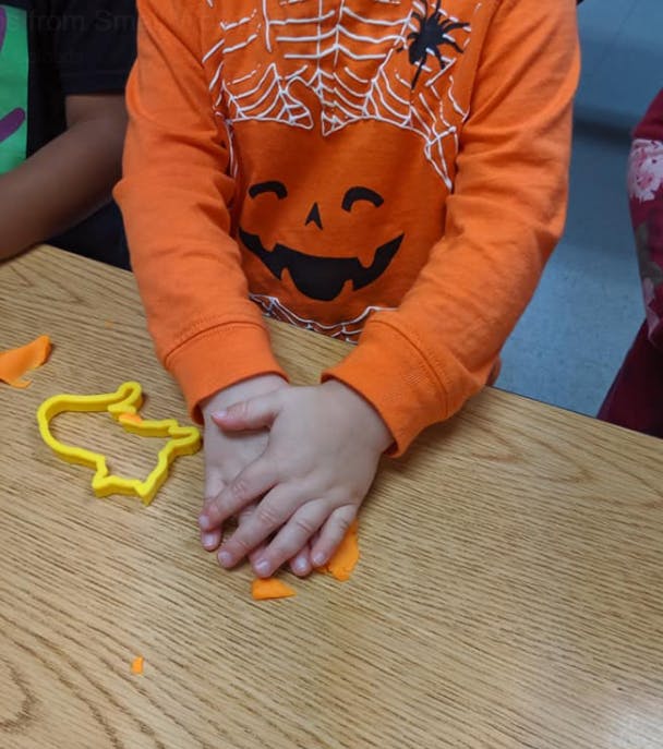 Child in Halloween shirt playing with orange playdough and cookie cutter