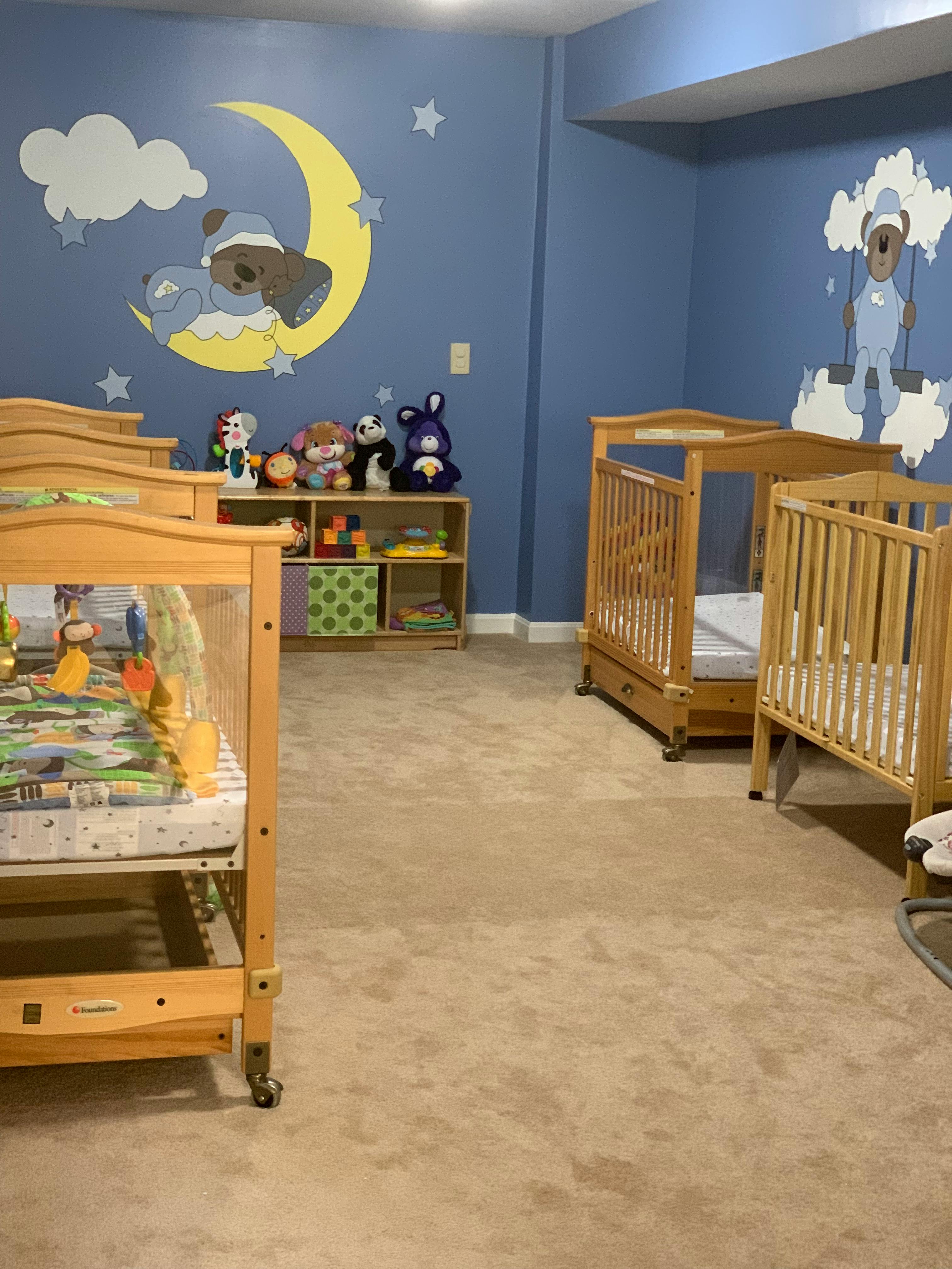 two empty wooden cribs in a room with blue walls and cartoon bear decals