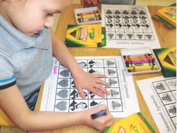 Child coloring a worksheet with crayons at a table with crayons