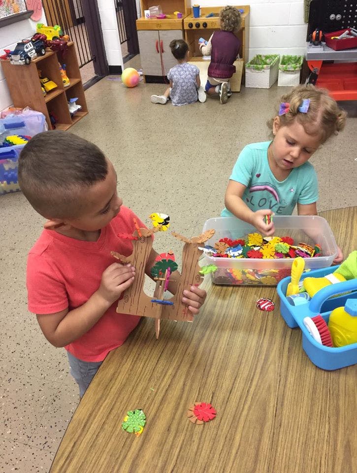 Child playing with a wooden toy, another child playing with small toys