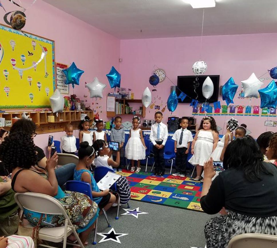 Children in formal attire standing in a room with adults watching
