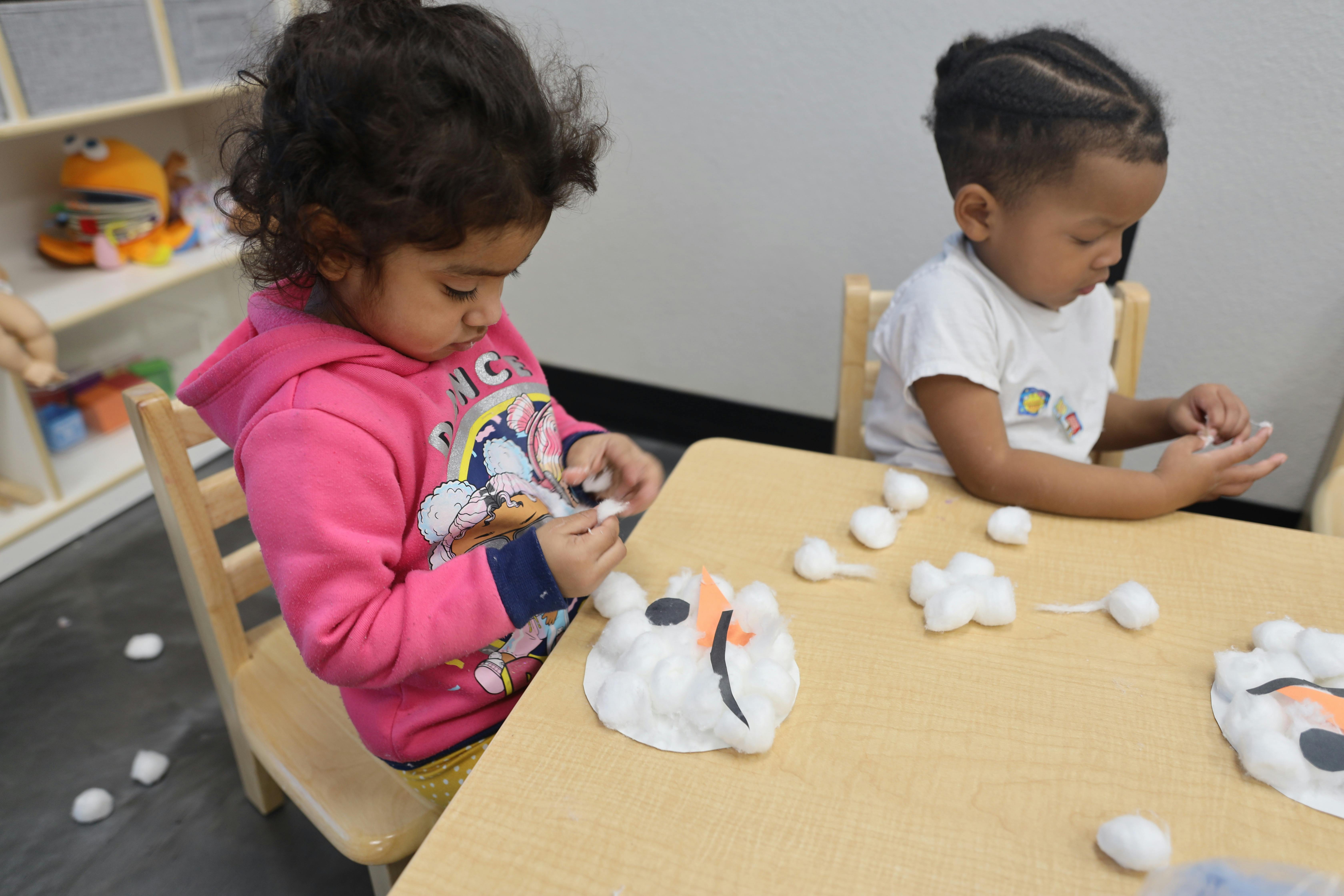 Two children doing a craft with cotton balls at a table