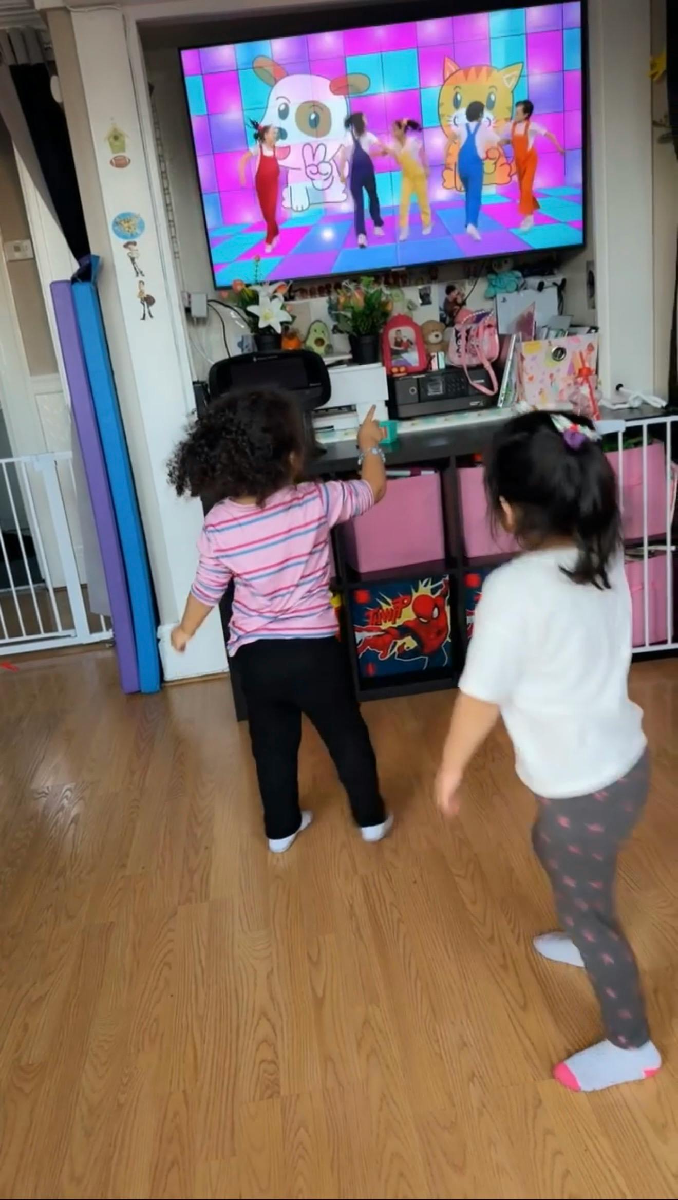 Two children dancing to a cartoon playing on a television