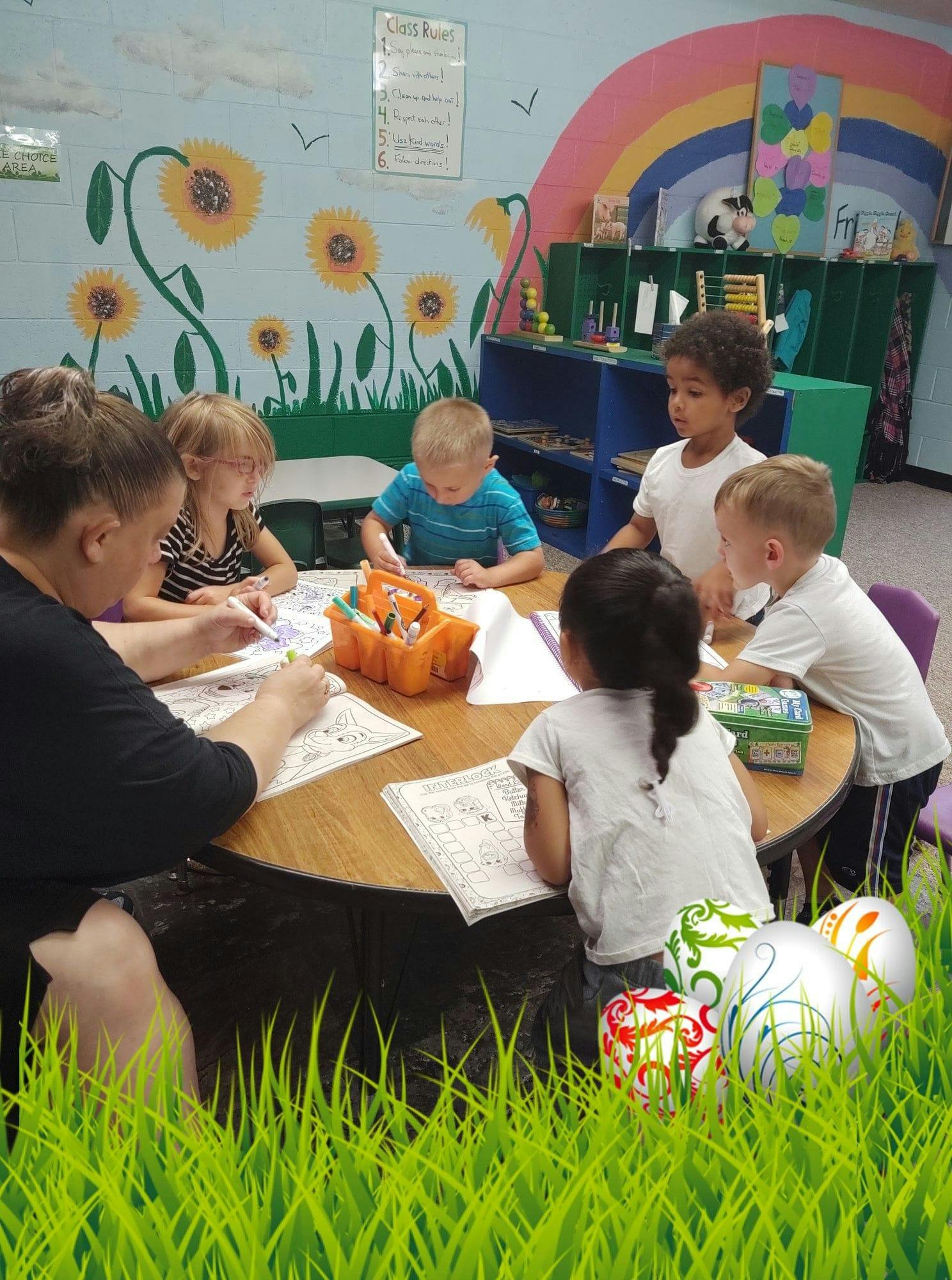 Adult and children sitting at a table, drawing or writing