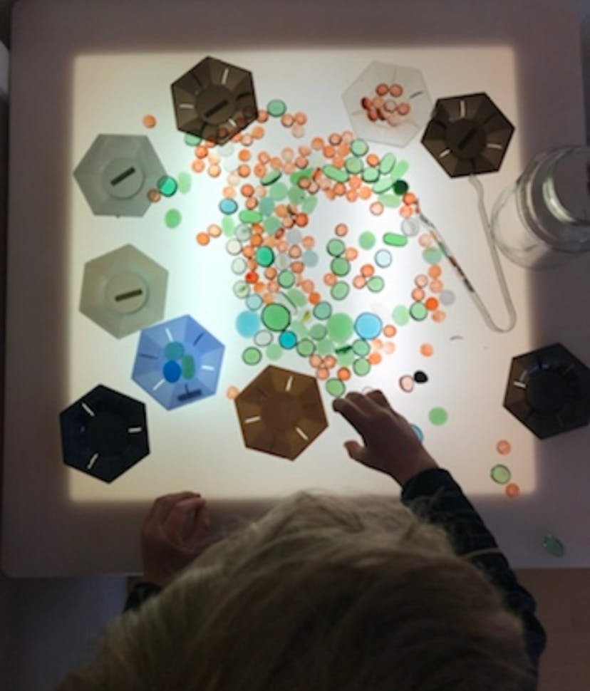 Child's hand reaching for colorful translucent shapes on a light table