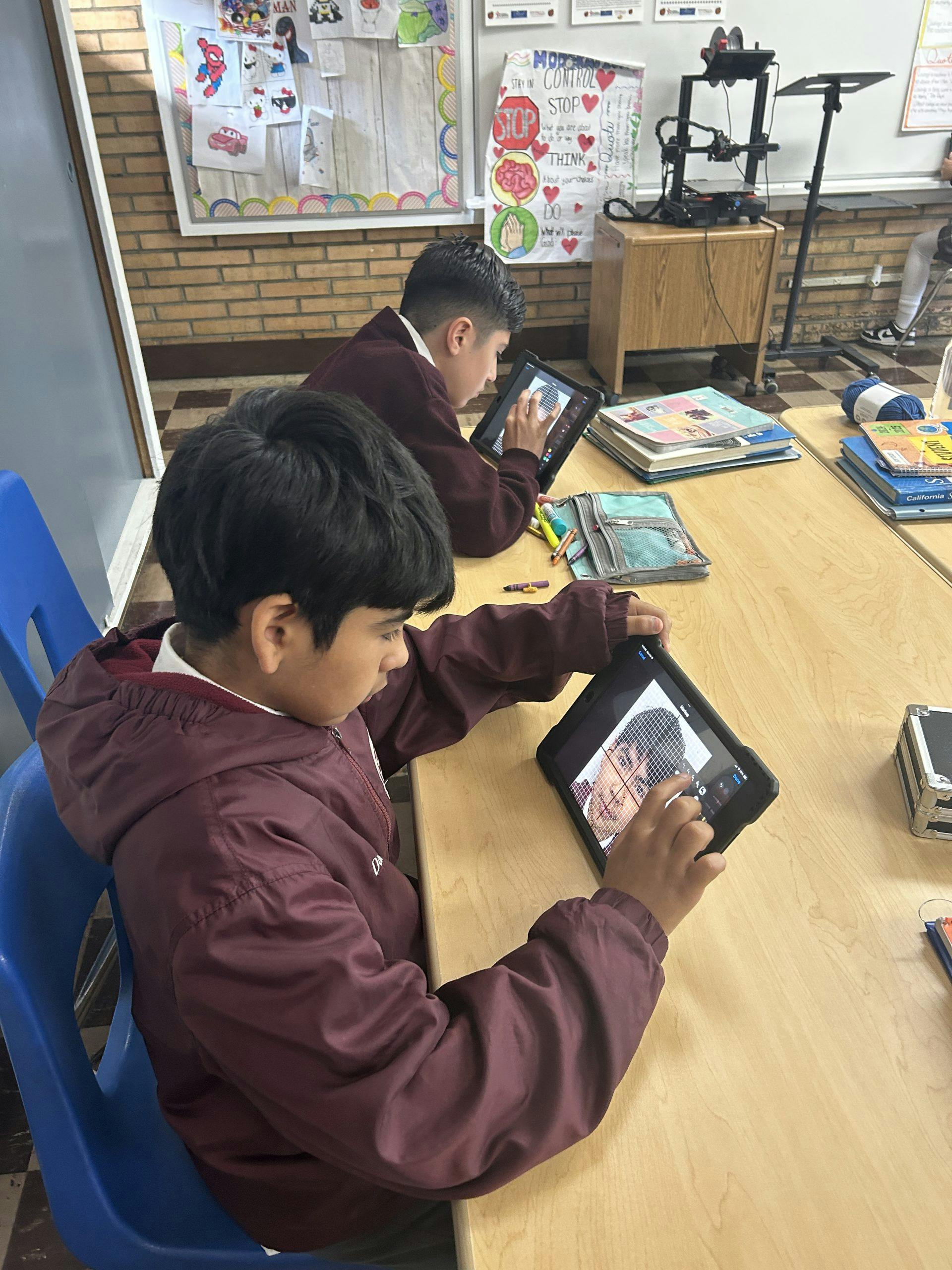 Two teens working on tablets at a desk in a classroom