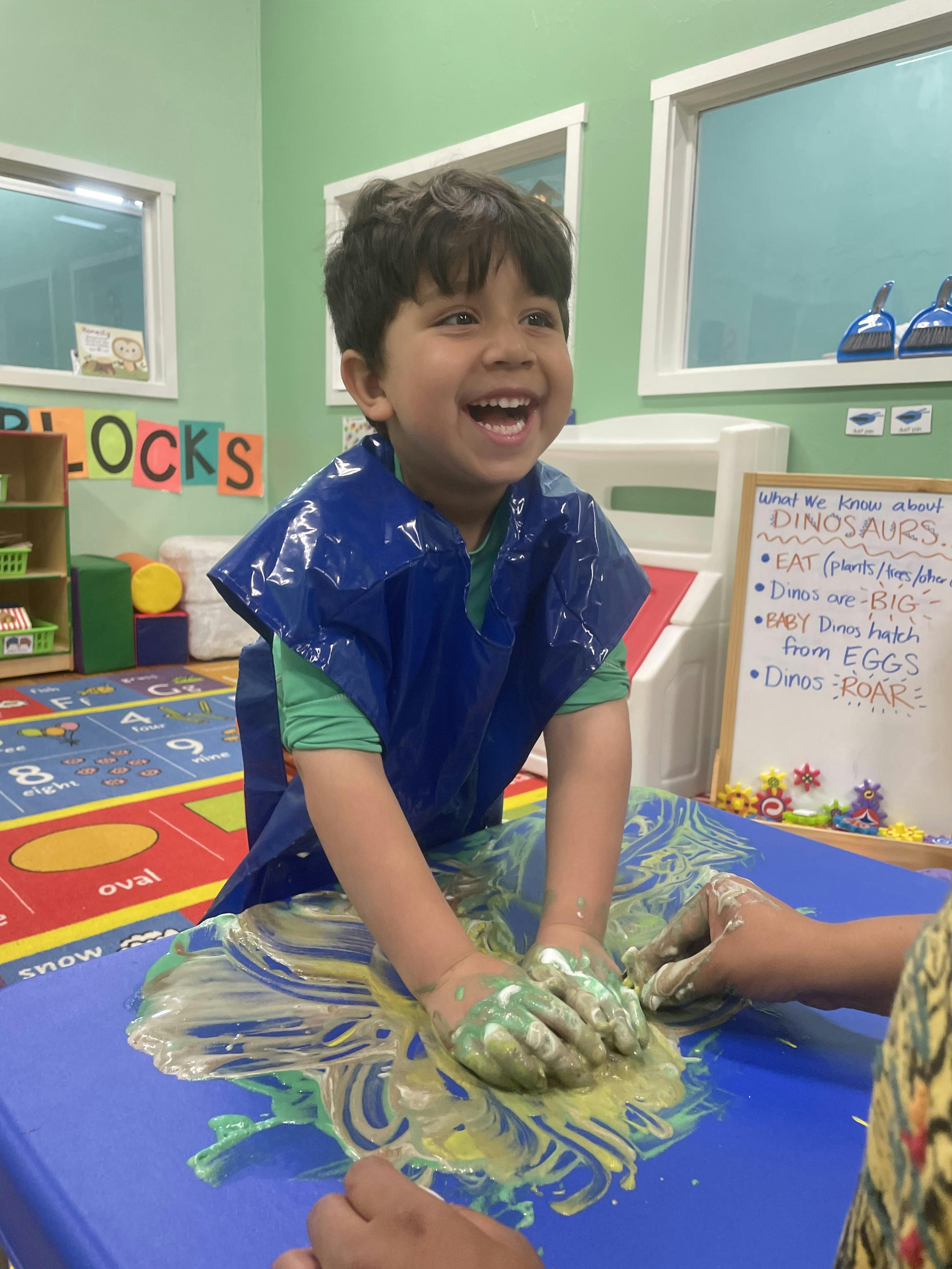 Child in a blue apron finger painting in a classroom