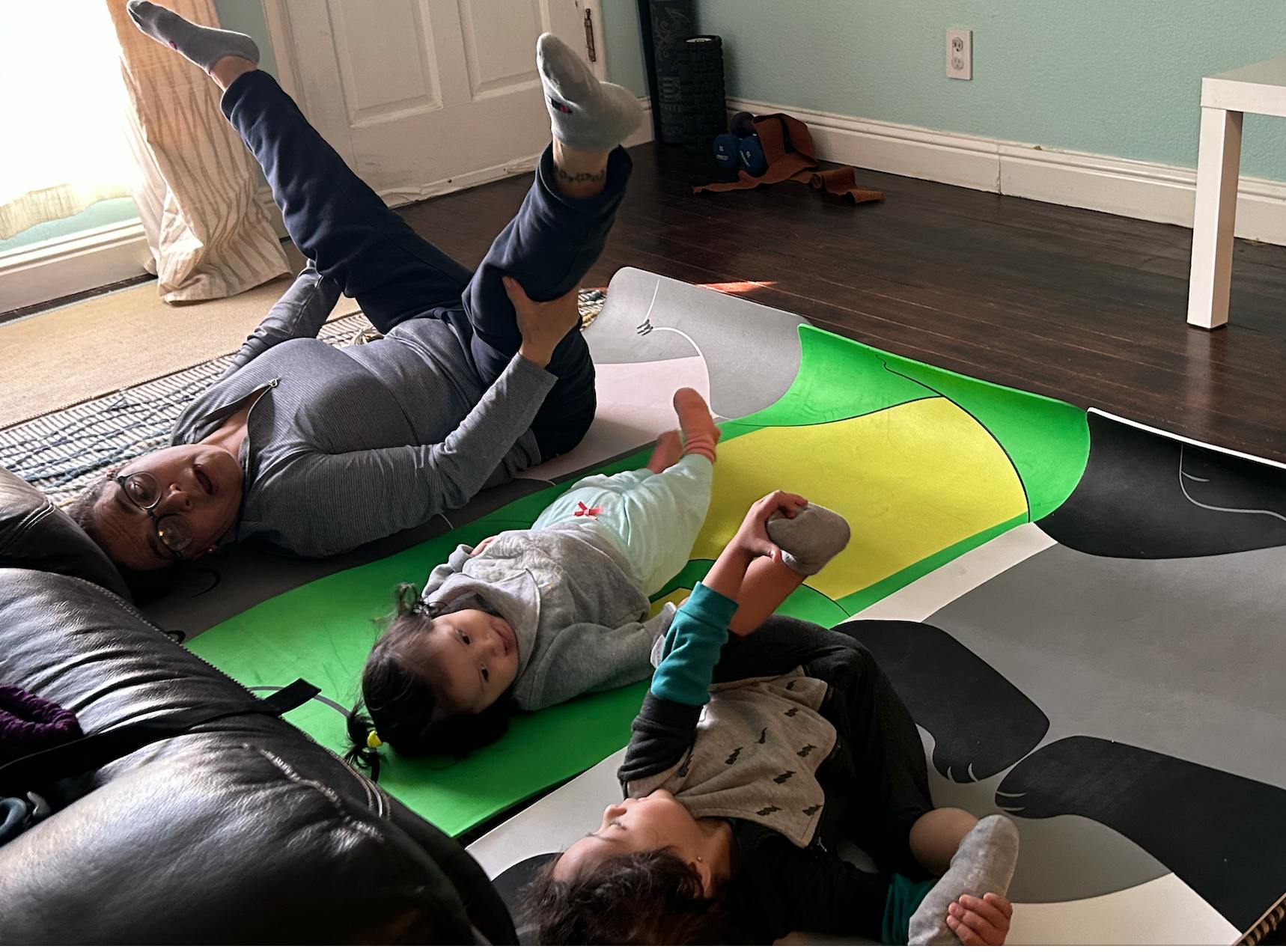 Person and two children lying on mats, person holding legs up