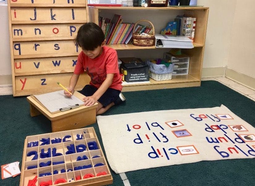 Child writing on paper on a small desk in a classroom