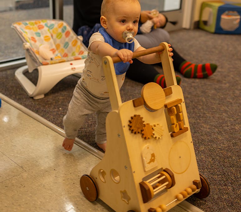 Child with pacifier holding onto a wooden activity walker