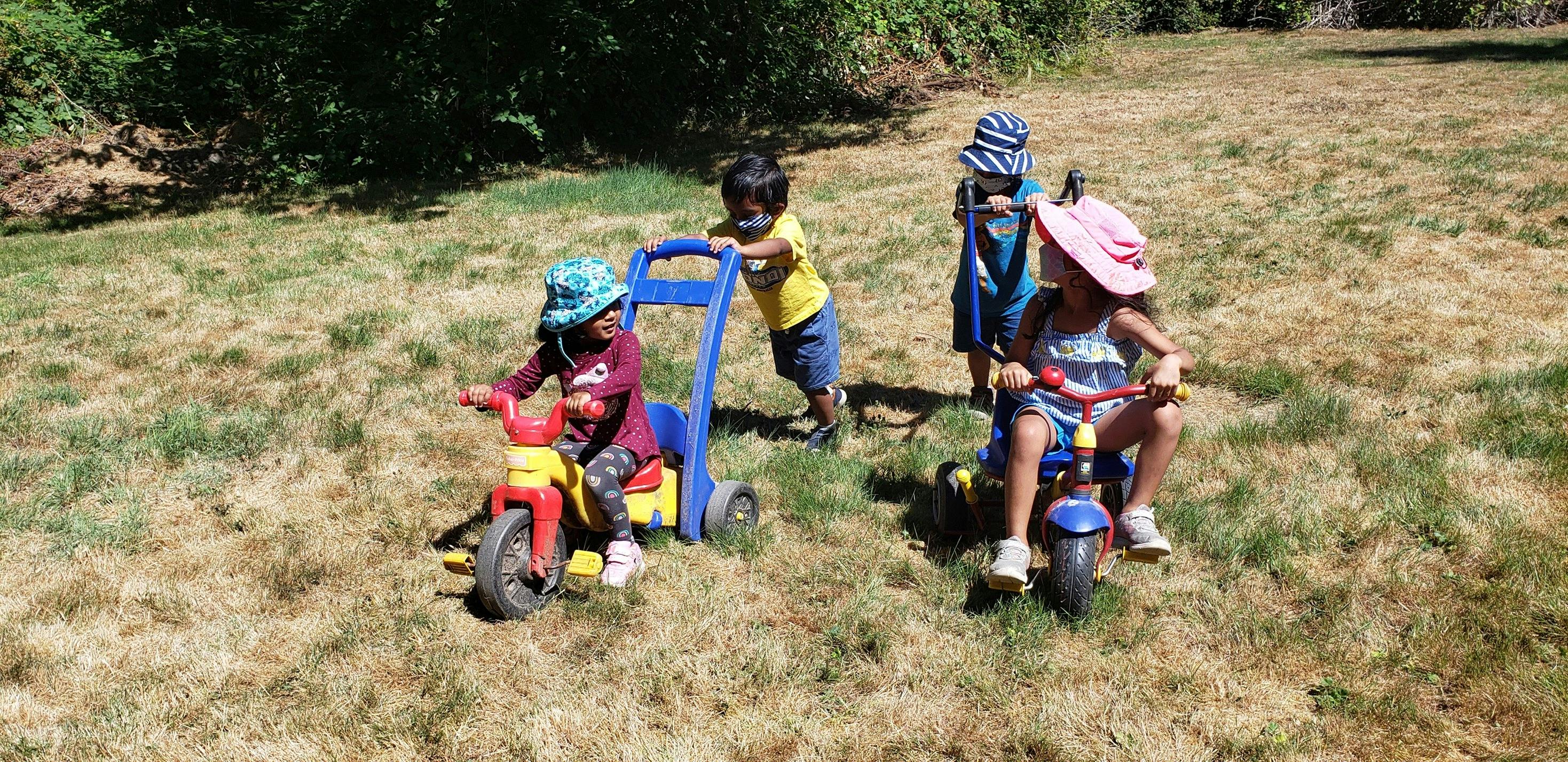 Children playing with ride-on toys and a push cart outdoors