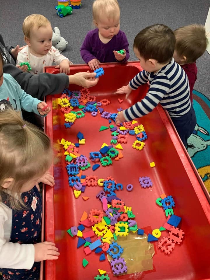 Children playing with colorful interlocking toys in a red bin