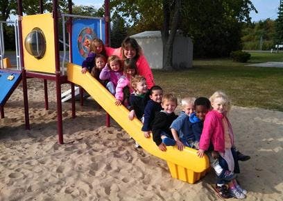 Person and multiple children sitting on a playground slide
