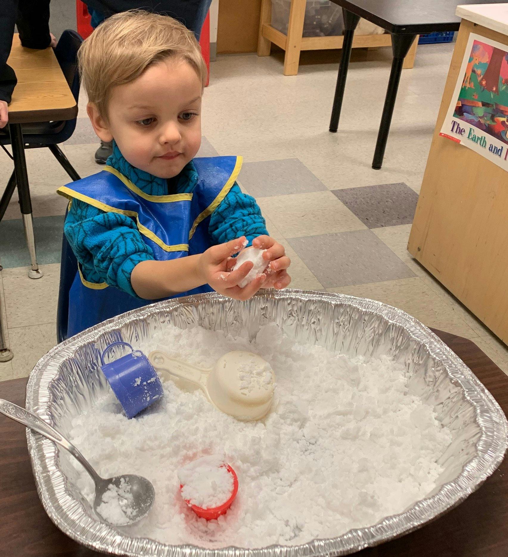 Child in an apron playing with white sensory material in a foil pan