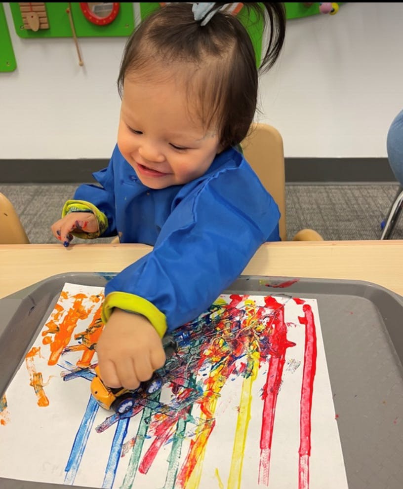 Child in a blue smock painting with a toy car